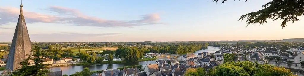 Montrichard Val de Cher au coucher du soleil, vue depuis les hauteurs : le clocher, les toits d’ardoise, le Cher et son pont, la campagne au loin.