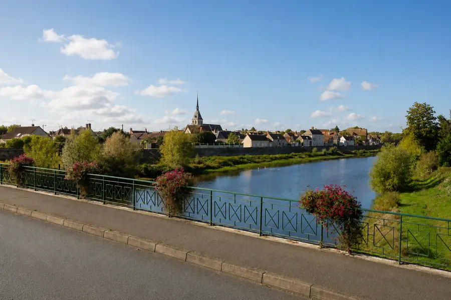 Selles-sur-Cher vue depuis le pont : le clocher de l’église au-dessus des toits du bourg, le Cher au premier plan, garde-corps fleuri.
