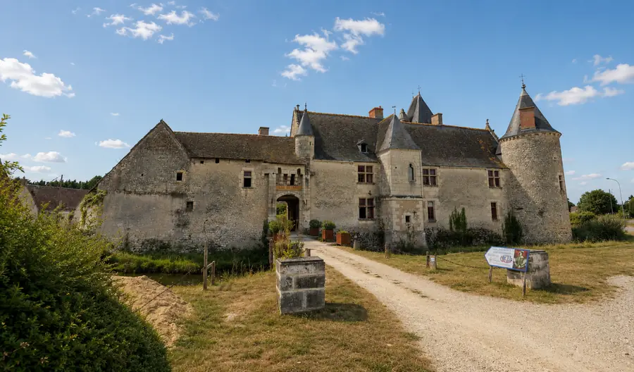 Le château de Chémery : corps de logis de pierre claire entouré de douves, flanqué d’une tour ronde à toit conique, allée de gravier menant au porche.