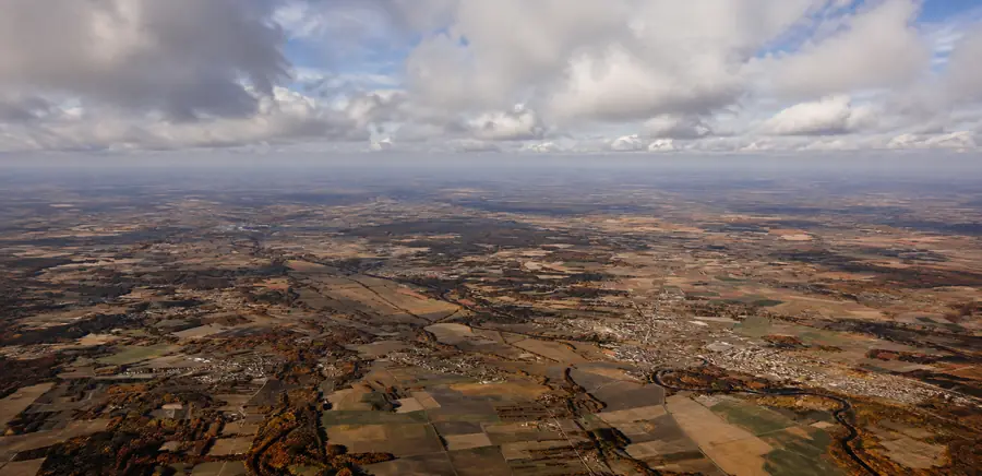 Vue aérienne du territoire : parcelles cultivées, bosquets, bourgs dispersés et le Cher traversant la plaine sous un ciel nuageux.